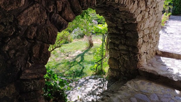 Un arc en pierre mène à un jardin où l’on trouve de la pelouse et des plantes.