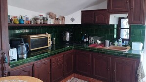 Une cuisine avec des meubles en bois foncé, un dosseret de carreaux verts et divers appareils de cuisine.