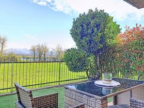 A patio with wicker furniture, a glass-top table, and a view of a green field and mountains. - Parma House by Interhome (Lonato del Garda)
