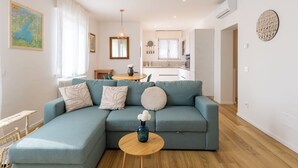 Een moderne woonkamer met een hoekbank, een houten salontafel en een eethoek op de achtergrond.