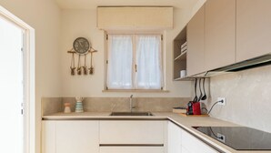 Een kleine keuken met een spoelbak, kastjes, een klok en een raam met gordijnen.