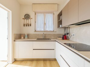 A compact kitchen with a sink, cabinets, a clock, and a window with curtains. - Lago di Luce by Interhome (Riva del Garda)