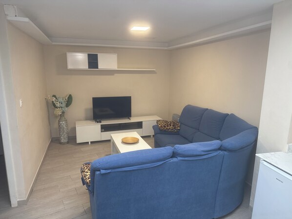 Een woonkamer met een bank, een televisie op een dressoir, een kleine tafel en een witte kast.