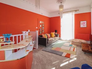 A living room with a red accent wall, a sofa with colorful cushions, a patterned rug, and a white bar area with blue glassware. - Tower Cottage (Nottingham)