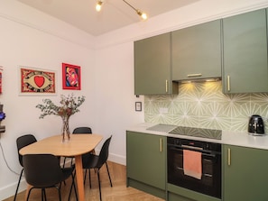 A modern kitchen with green cabinets, a white countertop, and a dining area with a wooden table and black chairs. - Tower Cottage (Nottingham)