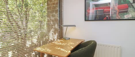 A room with a wooden desk, a green chair, a radiator, and a window with blinds.
