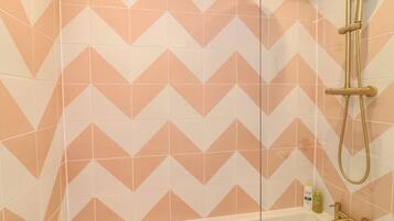 A shower with a geometric tile pattern, a handheld showerhead, and a bottle of shampoo.