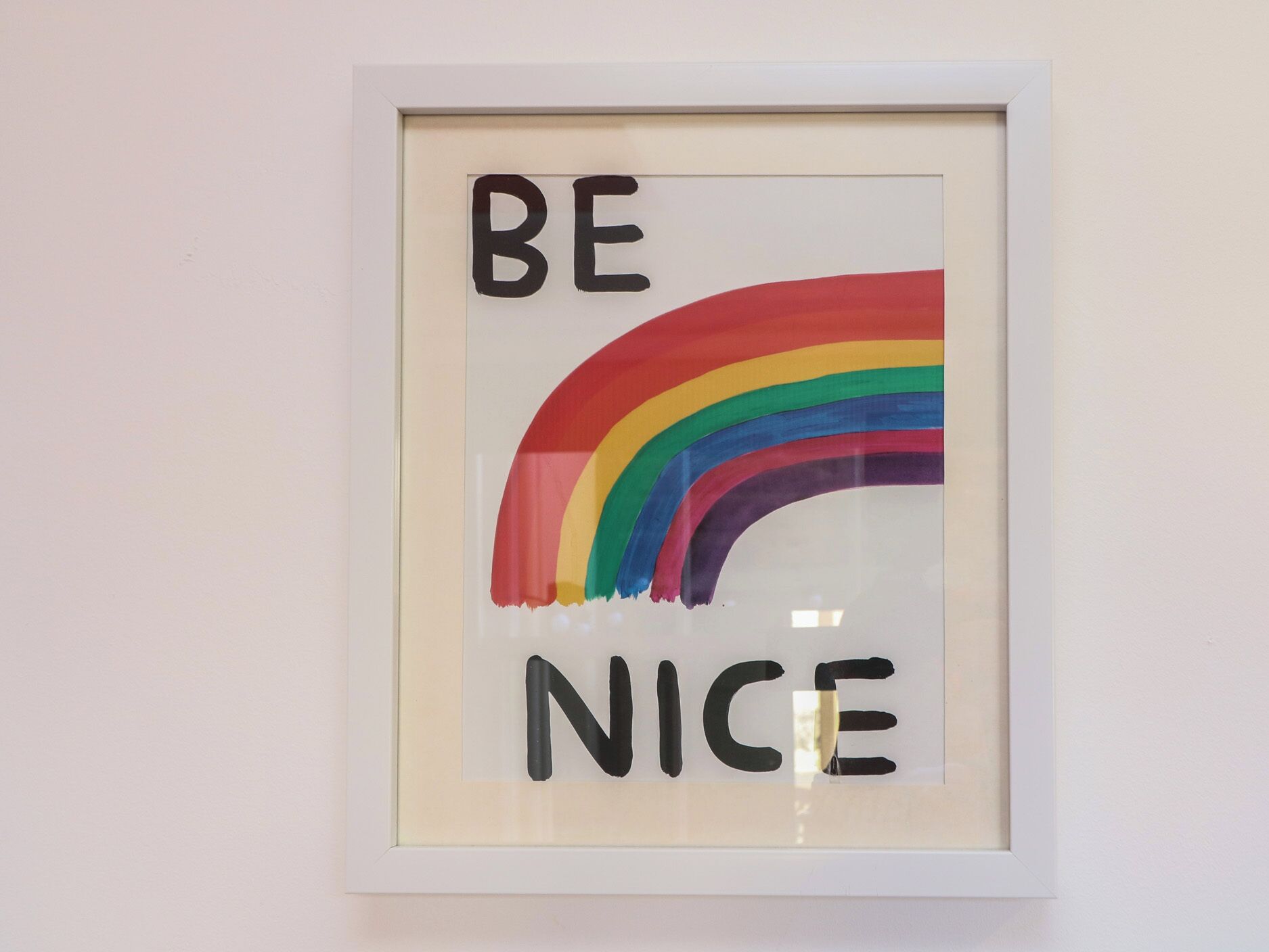 Uma obra de arte emoldurada com a frase 'BE NICE' e um arco-íris.