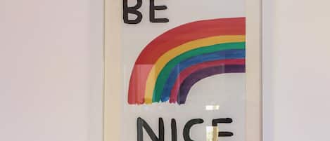 Uma obra de arte emoldurada com a frase 'BE NICE' e um arco-íris.