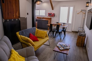 En stue med sofa, et bord med et brætspil, et køkken med mikrobølgeovn og et spiseområde med stole.