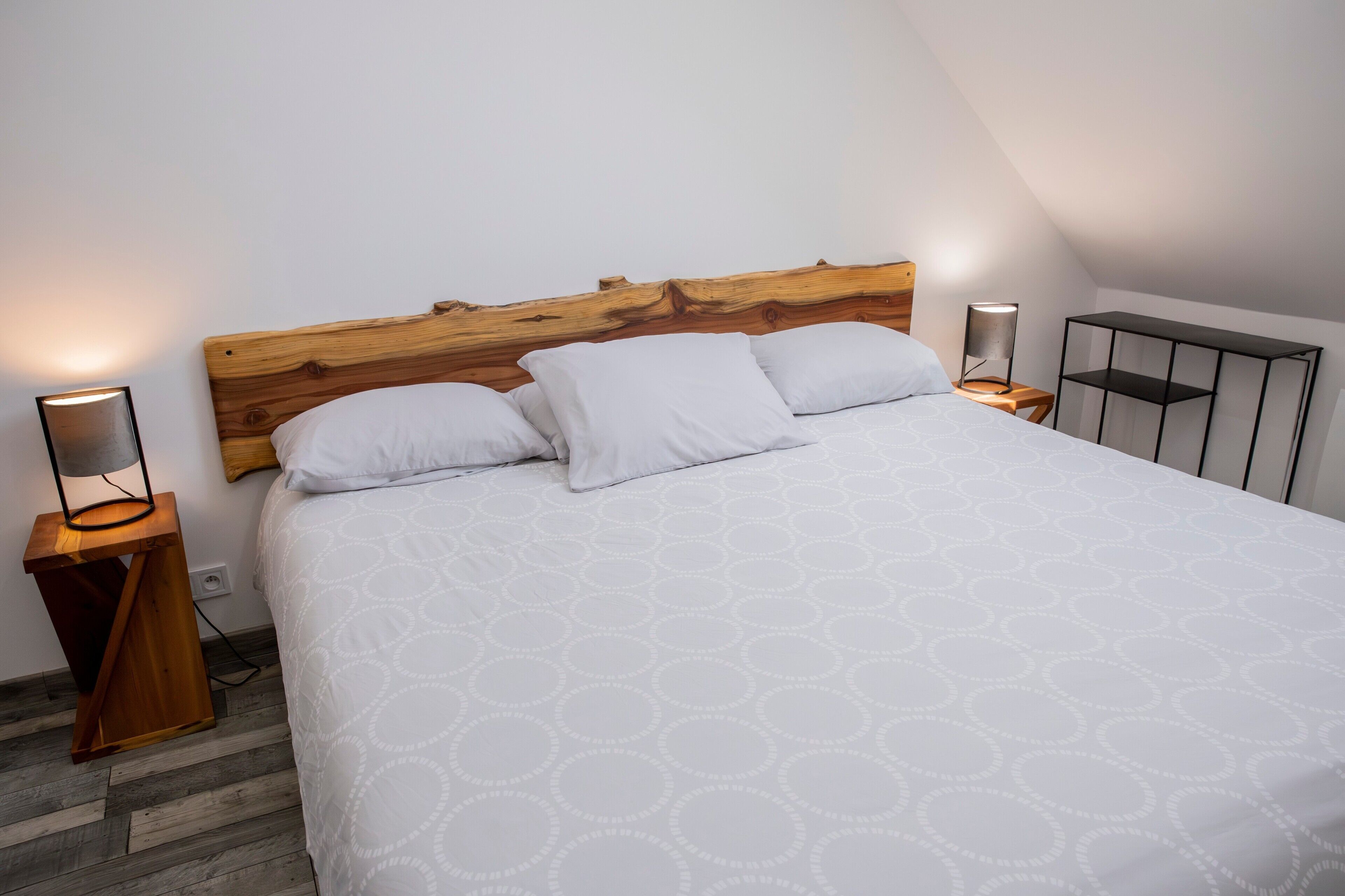 Une chambre à coucher avec une tête de lit en bois, une couvre-lit à motifs, deux tables de chevet avec des lampes et une étagère en métal.