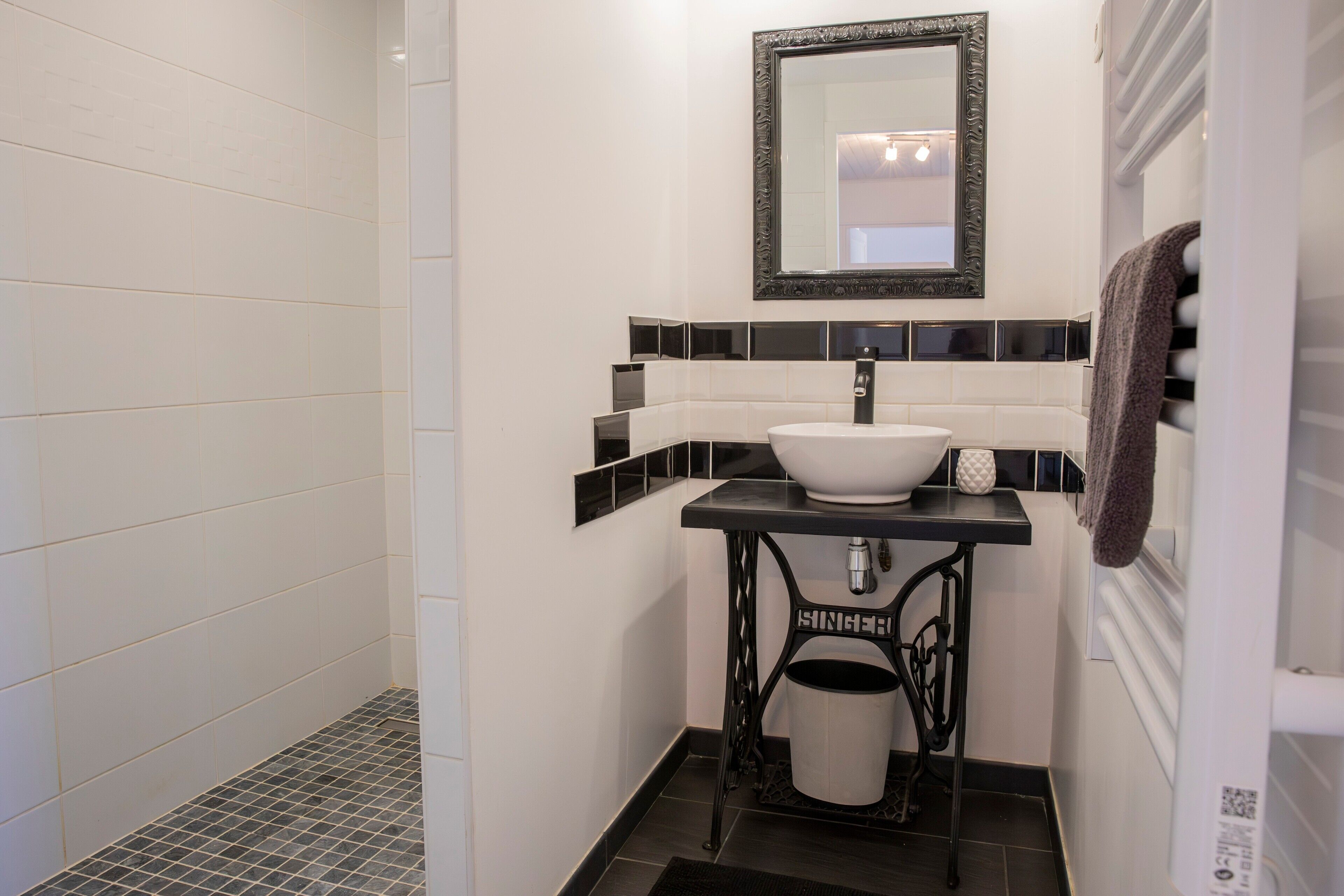 A bathroom with a white sink, black and white tiled walls, a mirror, and a black trash bin.