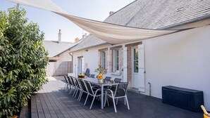Un patio con tavolo e sedie, un edificio bianco con tetto spiovente e un albero grande.