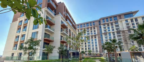A multi-story residential building with balconies, a landscaped garden, and a clear sky.