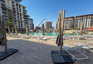 Área de piscina no terraço com espreguiçadeiras e guarda-sóis, cercada por edifícios altos em construção.