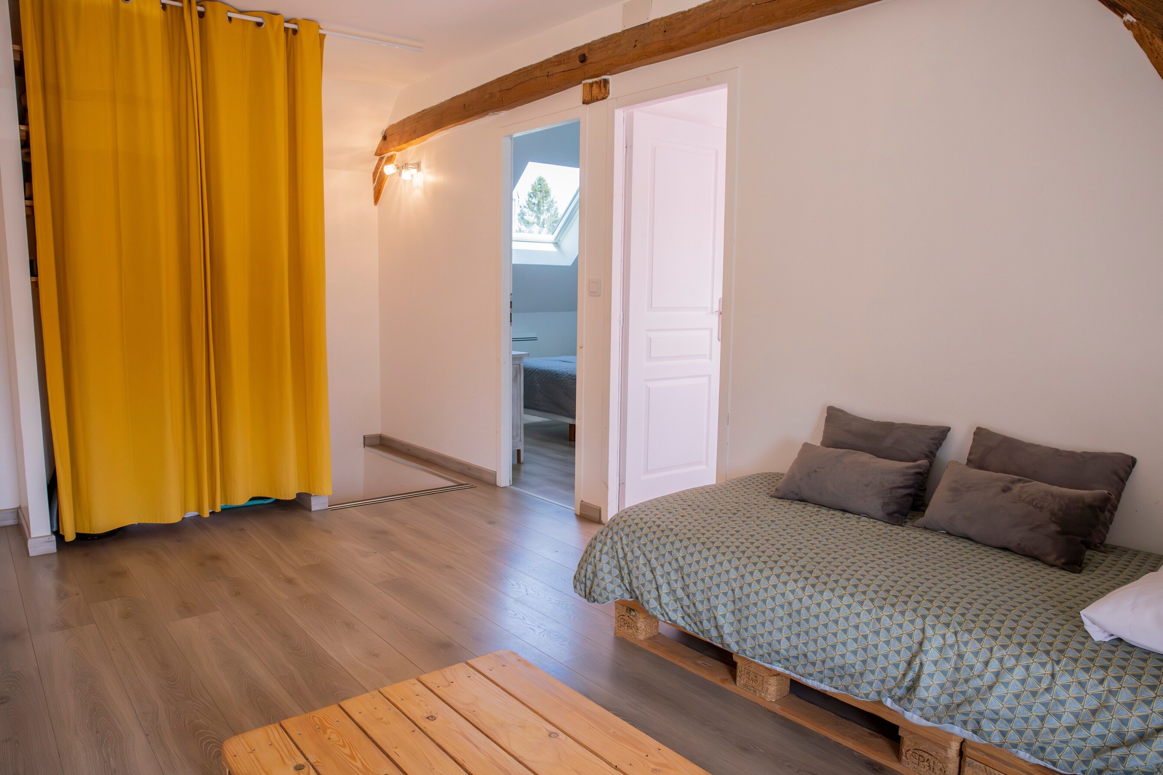 A bedroom with a bed, a wooden bench, and a yellow curtain.