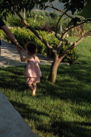 A child walking on a grassy path with trees and bushes in the background. - Armantanis Luxury Suites (Areopoli)