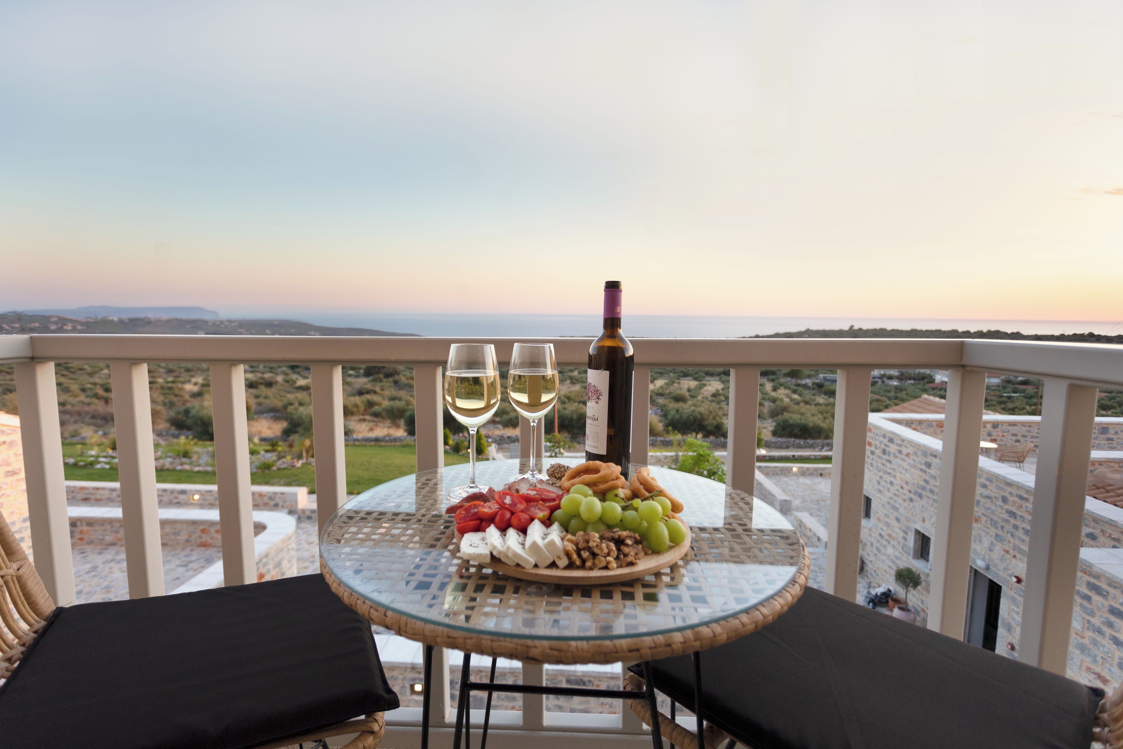 A balcony with a table set for two, featuring a cheese platter, grapes, nuts, and two glasses of white wine.