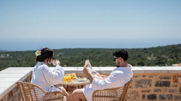 Dos personas sentadas a una mesa con vista al paisaje, un vaso de jugo de naranja y un periódico.
