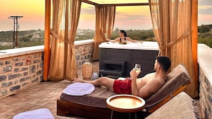A couple relaxing on a rooftop terrace with a hot tub, a stone wall, and a sunset view. - Armantanis Luxury Suites (Areopoli)