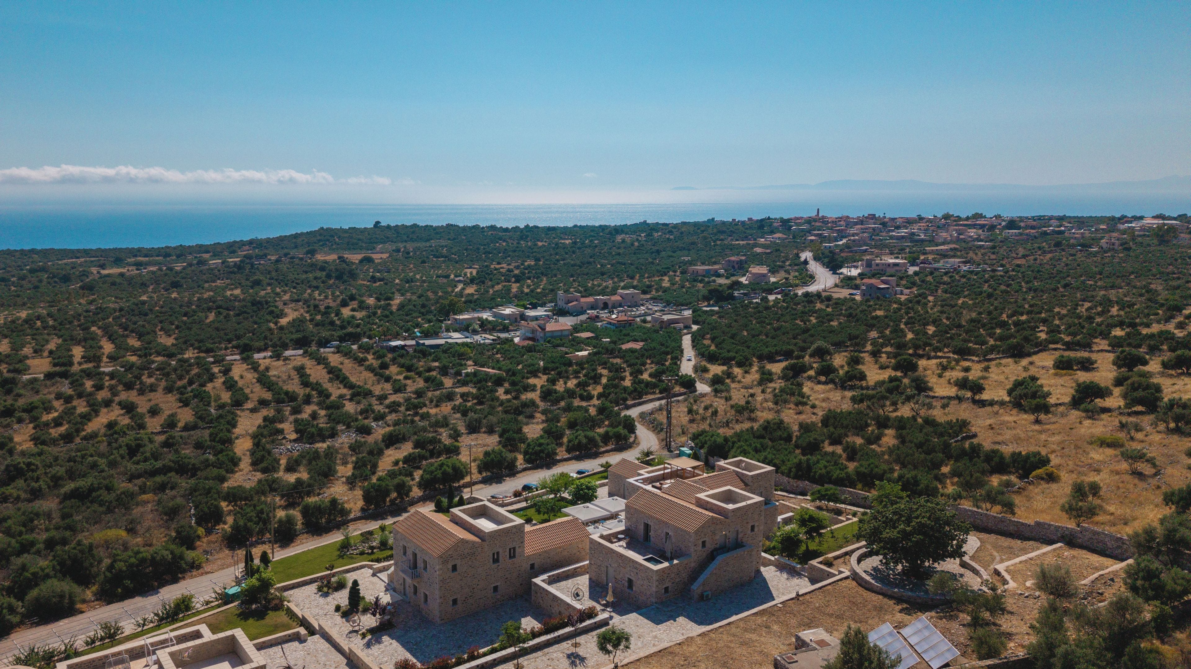 Vista aérea de un complejo histórico de edificios de piedra con un patio, rodeado por un paisaje rural y un telón de fondo costero.