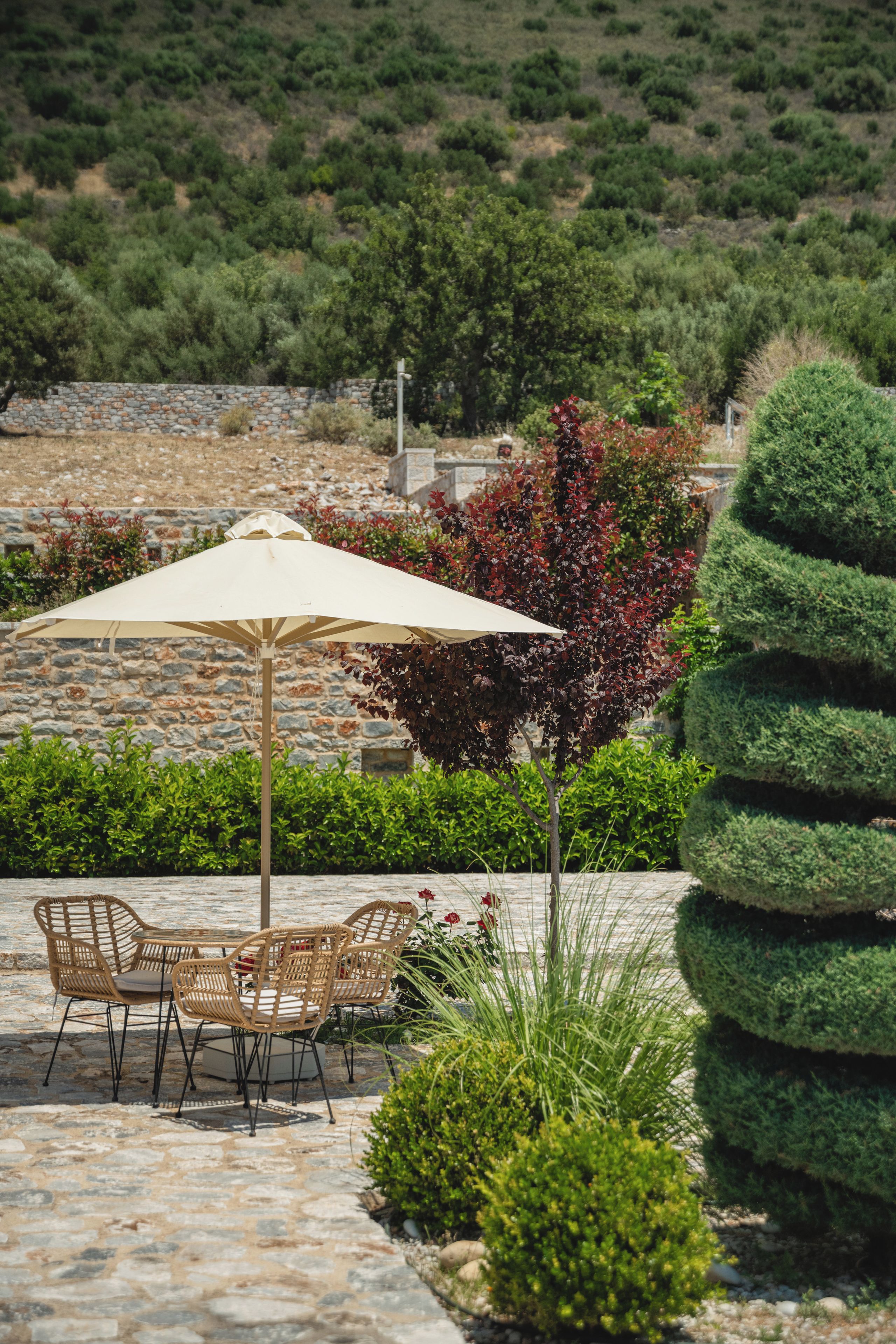 An outdoor seating area with a table and chairs, a large umbrella, and a stone wall.