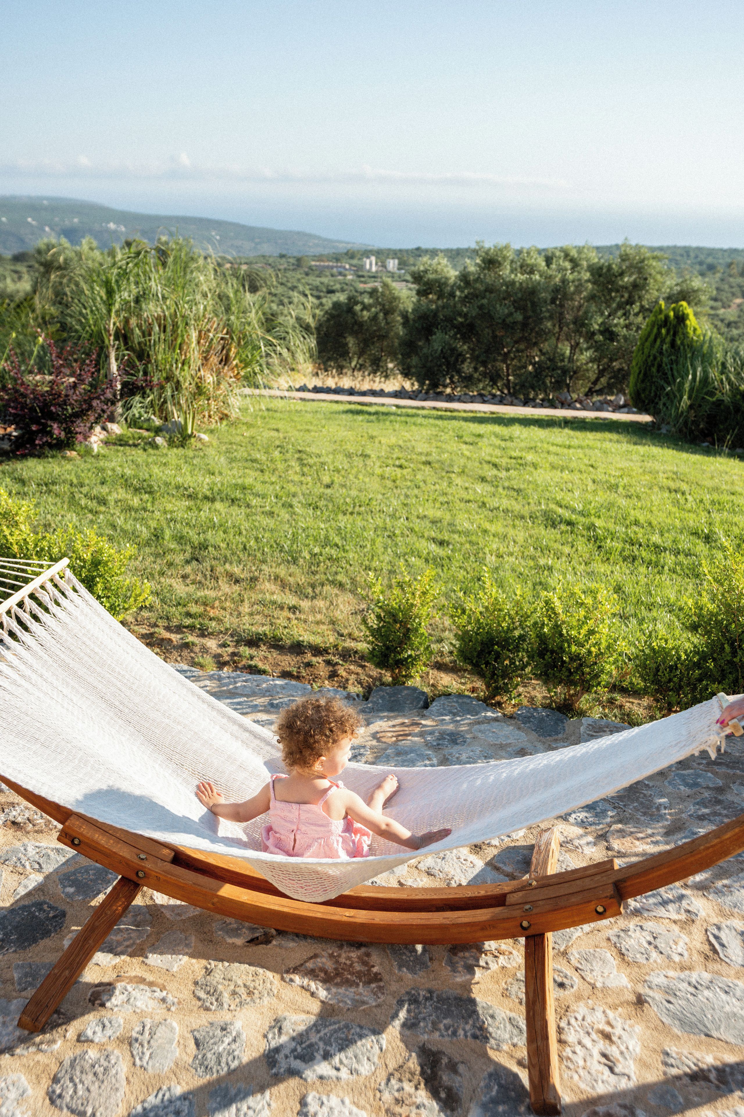 A hammock chair on a stone patio overlooking a grassy landscape with trees and a distant view of hills.
