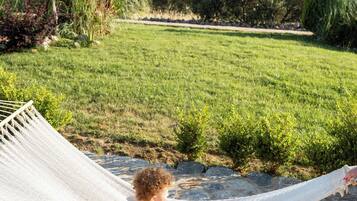 A hammock chair on a stone patio overlooking a grassy landscape with trees and a distant view of hills.