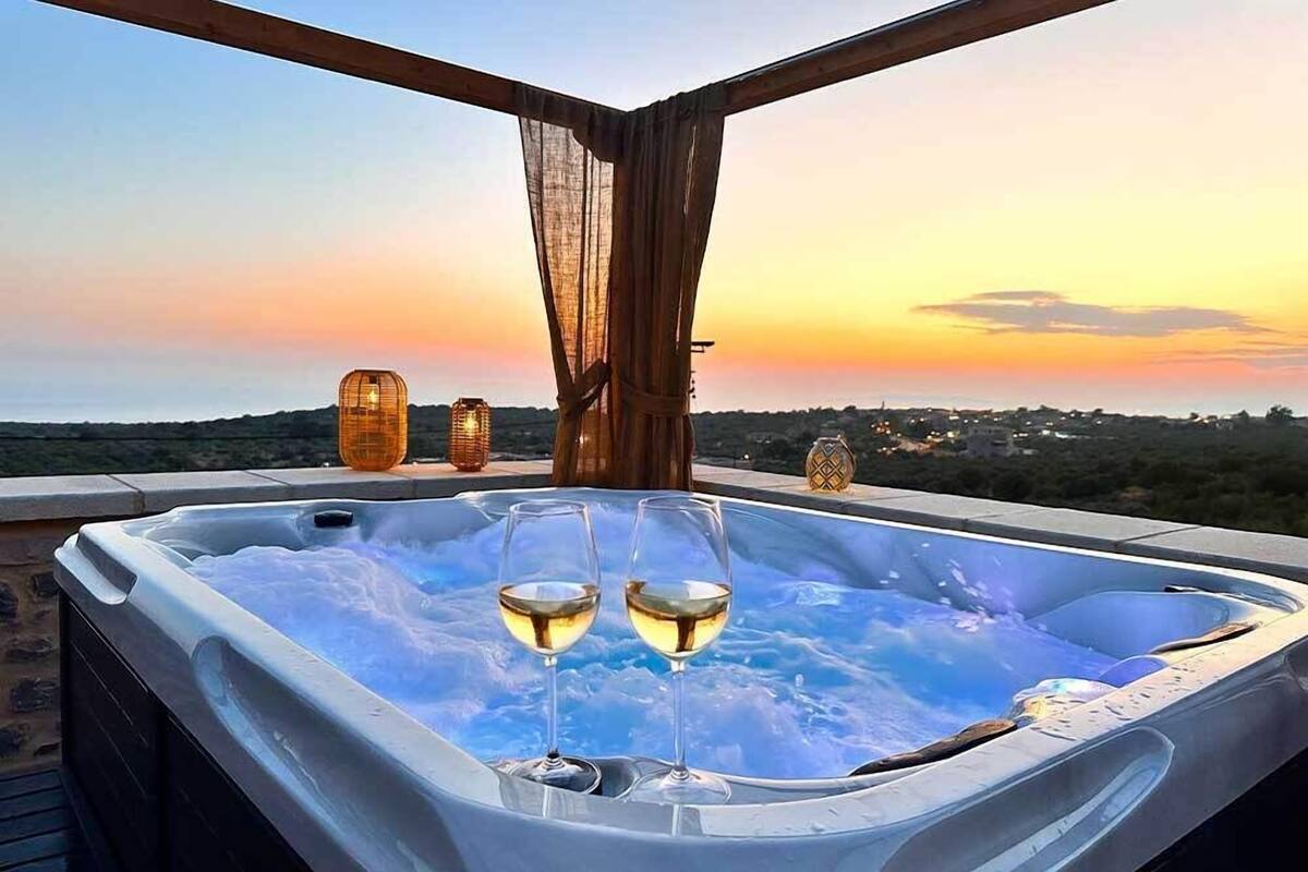 Un jacuzzi con dos copas de vino, vistas al atardecer y faroles decorativos.