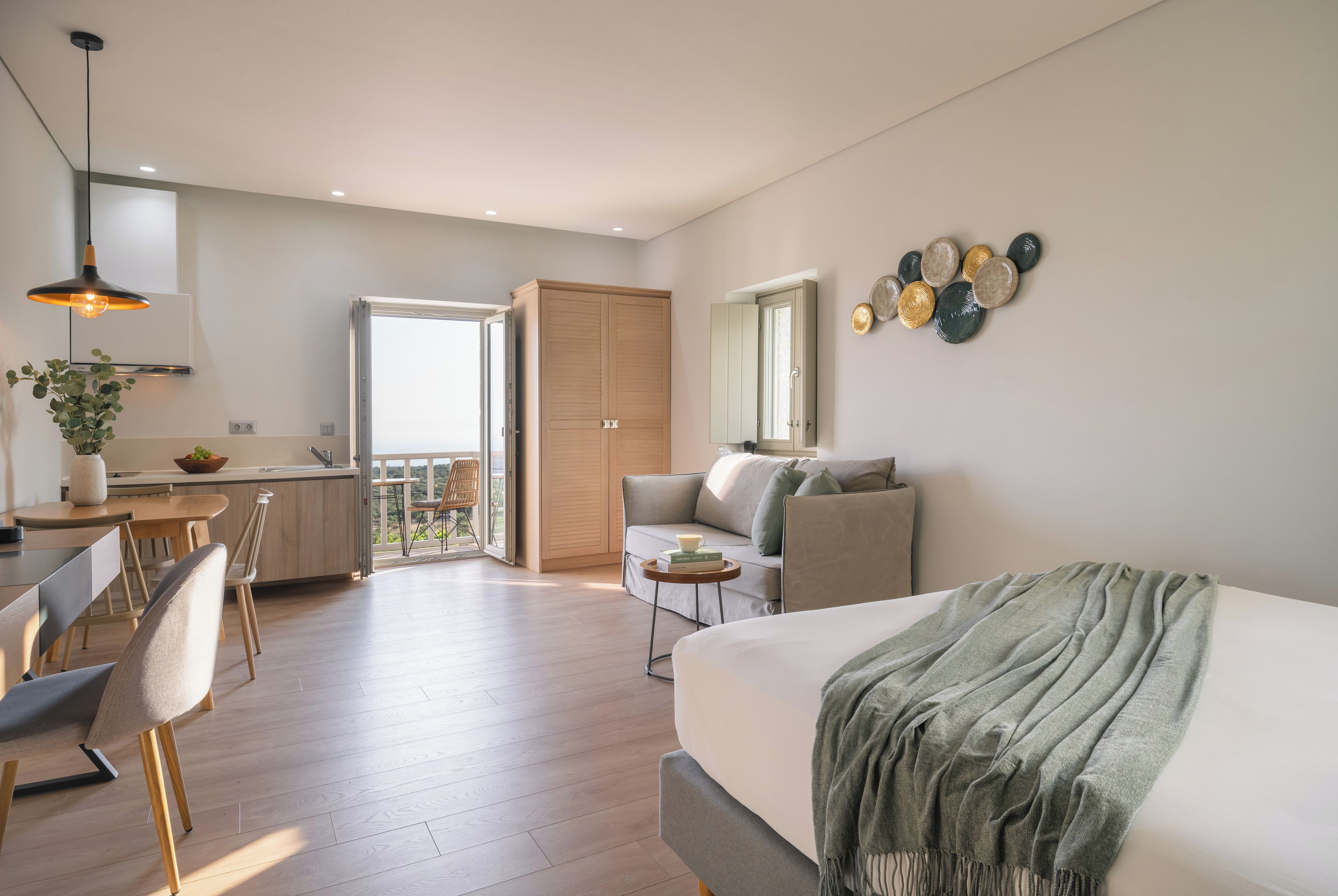 A modern bedroom with a large bed, a dining area with a table and chairs, a kitchen with a sink and cabinets, and a balcony with a view.