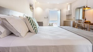 A modern hotel room with a large bed, a dining area, and a view of the outdoors. - Armantanis Luxury Suites (Areopoli)