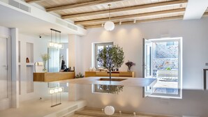 A modern interior with a central reflective surface, wooden beams, a large window, and a plant. - Armantanis Luxury Suites (Areopoli)