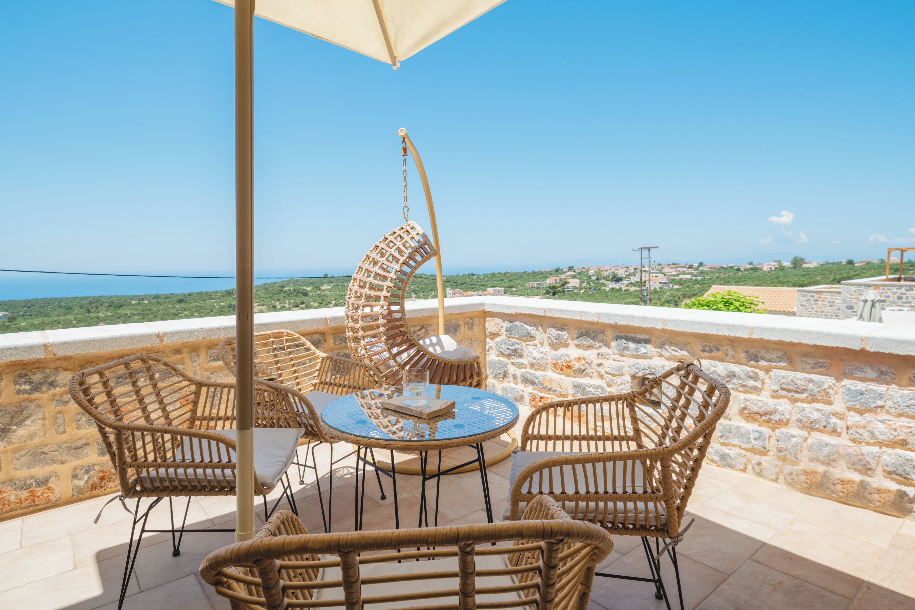 Una terraza con mobiliario de mimbre y una mesa, con vistas a un paisaje costero.