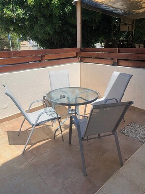 A round glass table with metal chairs, a wooden bench, and a tiled patio. - Kings Beach Townhouse (Paphos)