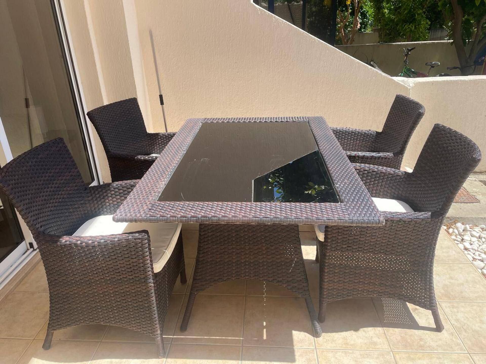 Una mesa de vidrio cuadrada con cuatro sillas de mimbre, cada una con un cojín.