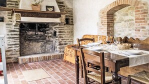 Een rustieke eethoek met een bakstenen openhaard, een houten tafel en stoelen.