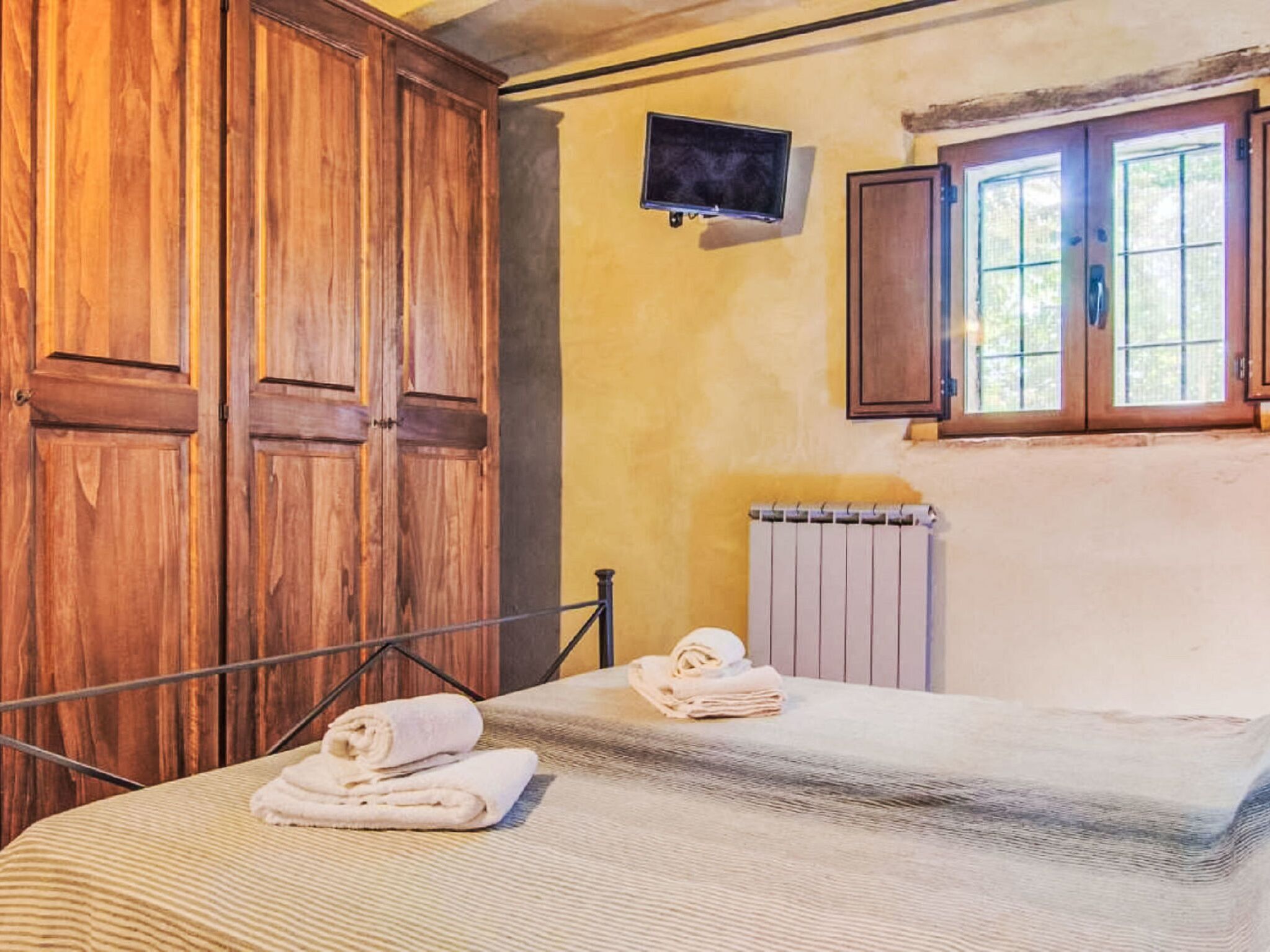 A room with a bed, wooden wardrobe, a radiator, and a window.