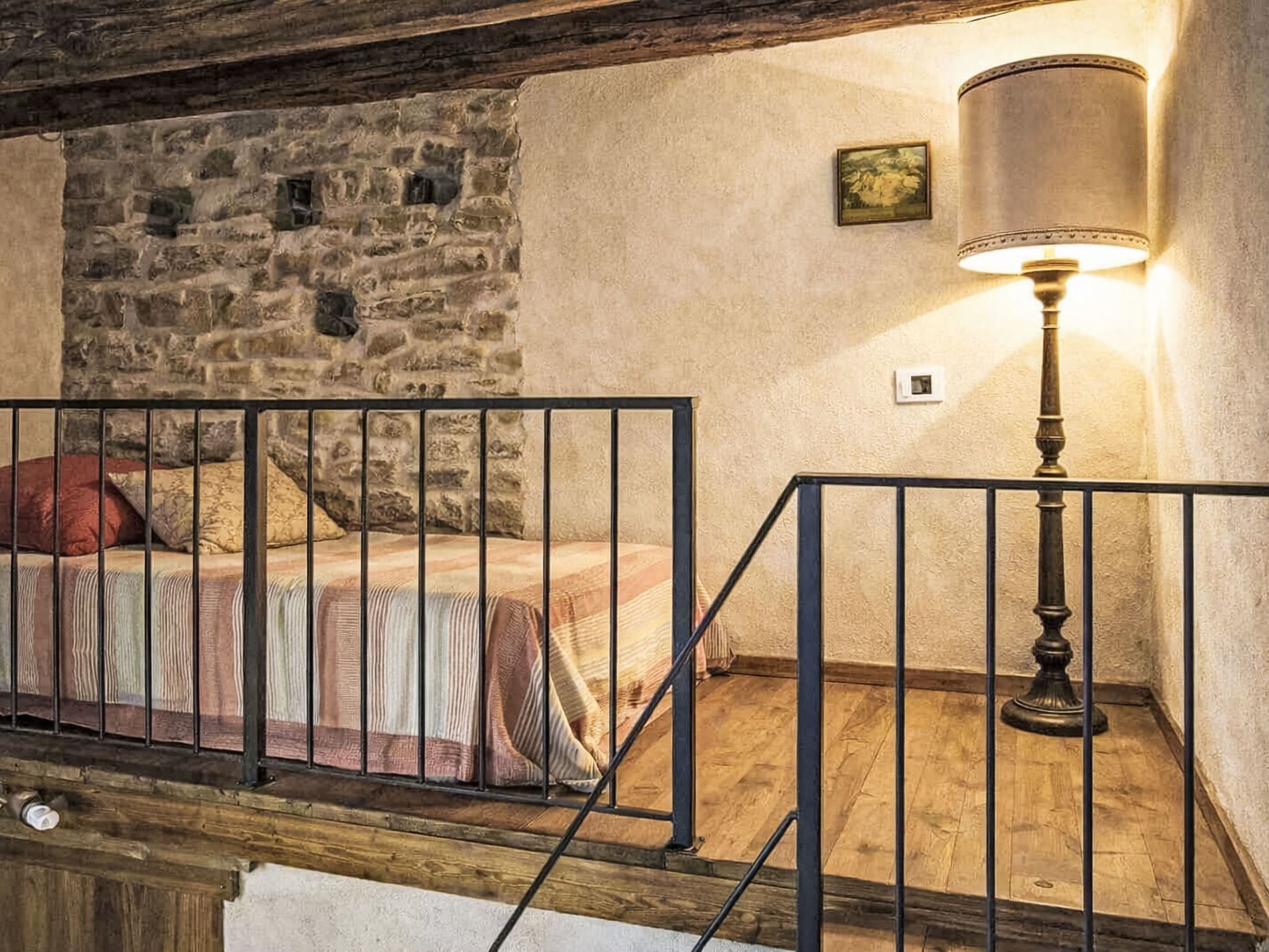 Una camera da letto con parete in pietra, un letto con copriletto decorato, un comodino e una lampada da terra.
