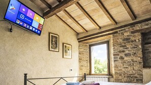 A bedroom with a bed, a TV mounted on the wall, a window, and stone walls. - La Collina degli Ulivi by Interhome (Perugia)