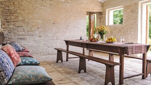 A rustic room with a brick wall, a wooden bench, a table with a plaid tablecloth, and colorful pillows. - La Collina degli Ulivi by Interhome (Perugia)