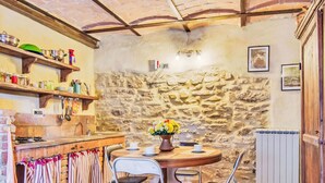 A rustic kitchen with stone walls, wooden shelves, and a round table with chairs. - La Collina degli Ulivi by Interhome (Perugia)