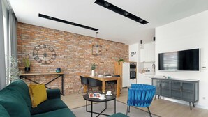 Un espacio habitable moderno con pared de ladrillo, comedor, sofá, televisión y cocina.