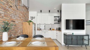 Una cocina moderna con armarios blancos, pared de ladrillo y comedor con mesa de madera para dos.