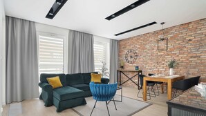 Una sala moderna con un sofá modular, una mesa de comedor con sillas, un sillón azul y una pared de ladrillo.