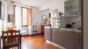 Cozinha moderna com piso de madeira, área de refeições com mesa e cadeiras, e janela com cortinas.