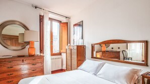 Quarto de hotel com cama, penteadeira, espelho e janela com cortinas.