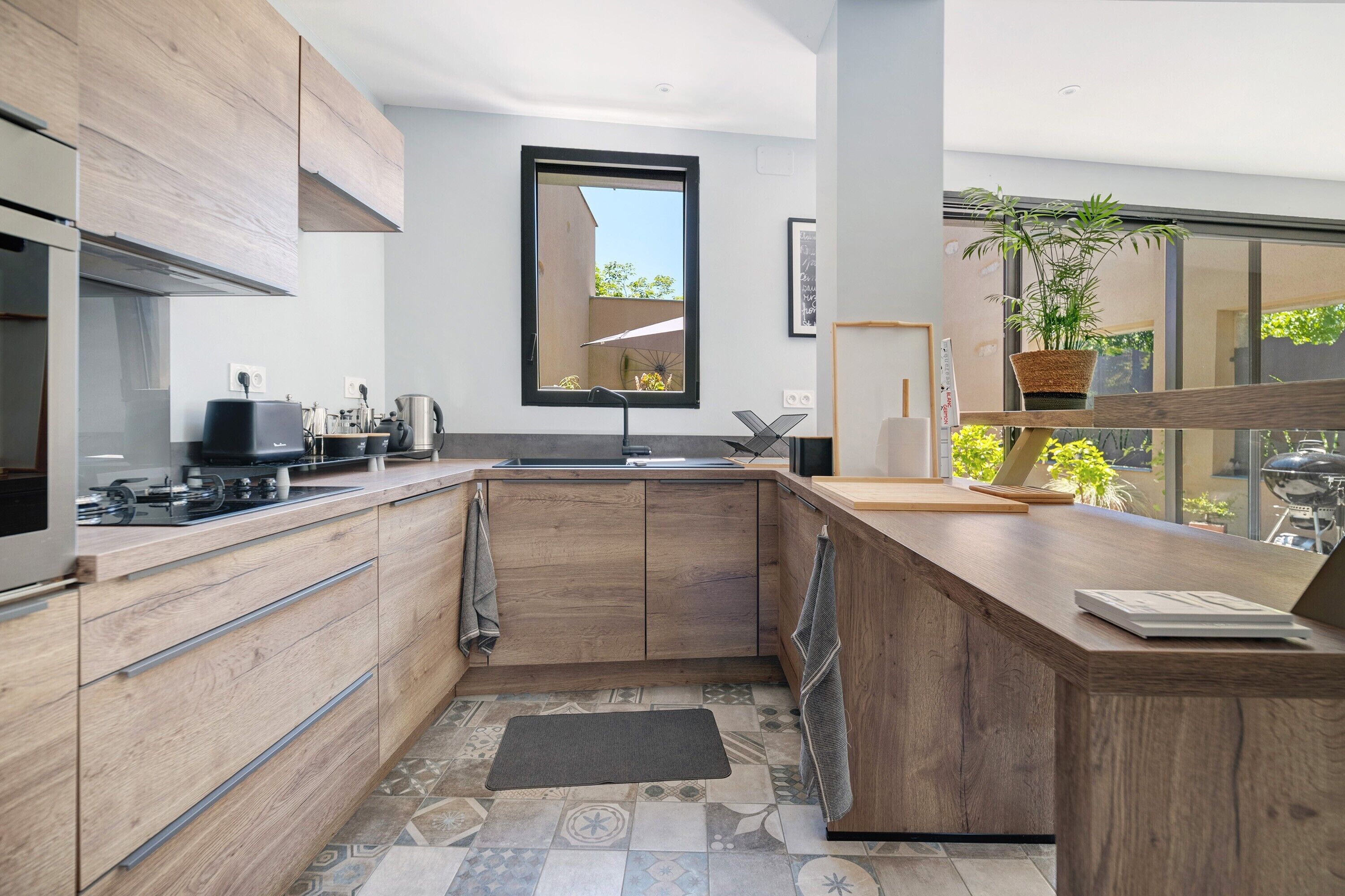A modern kitchen with wooden cabinets, a built-in stove, and a large window.