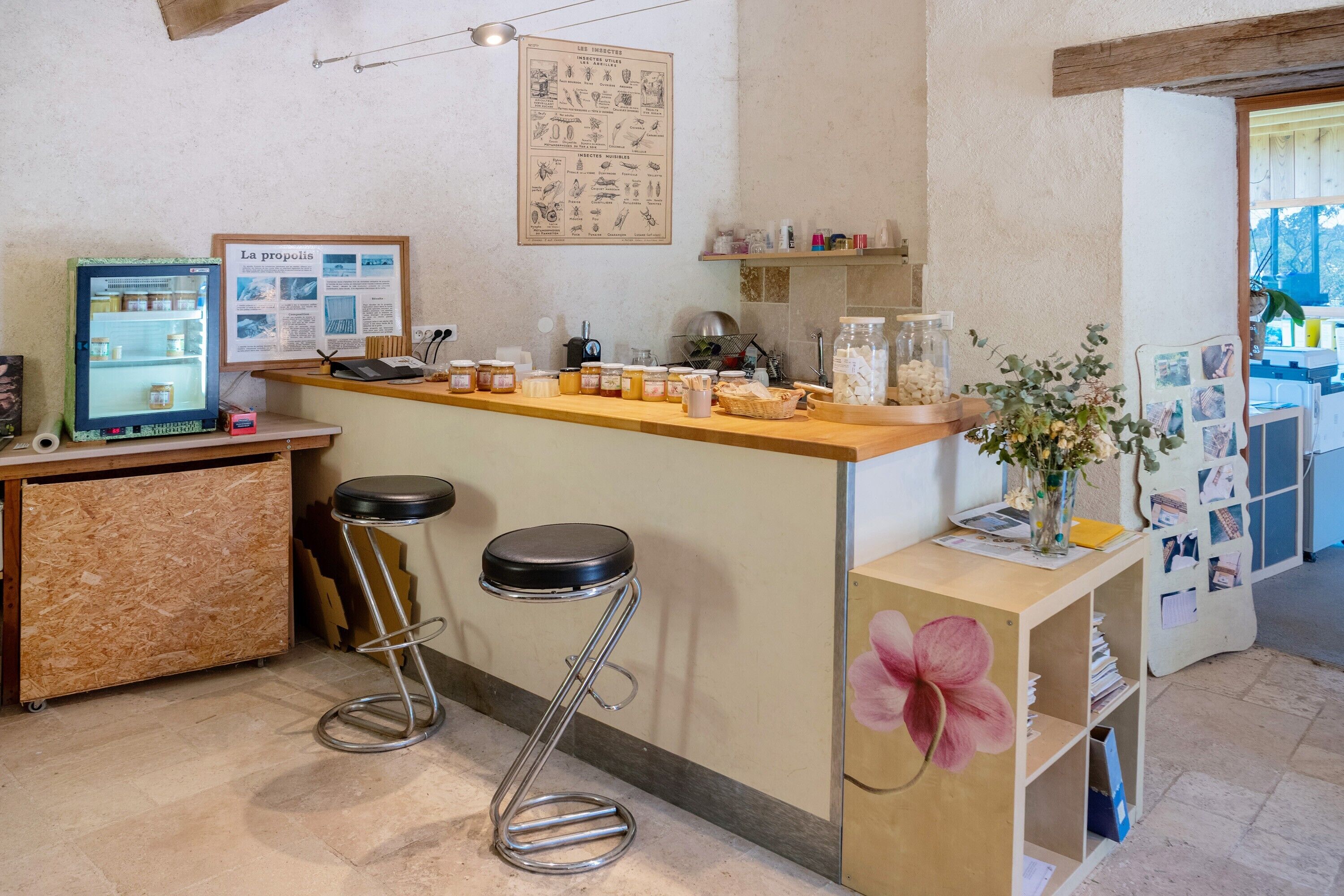 Un'area bar con sgabelli, un frigorifero, una bacheca con il menu e una decorazione floreale.