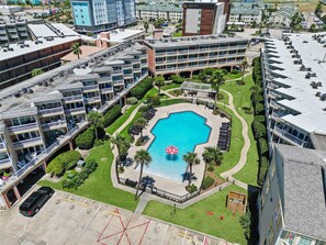 Ein mehrstöckiges Hotel mit einem zentralen Schwimmbad, Sitzgelegenheiten im Freien und einem Parkplatz.
