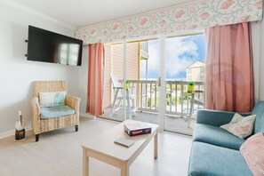 Ein Wohnzimmer mit Fernseher, Korbsessel, Sofa, Tisch und einem Balkon mit Blick.
